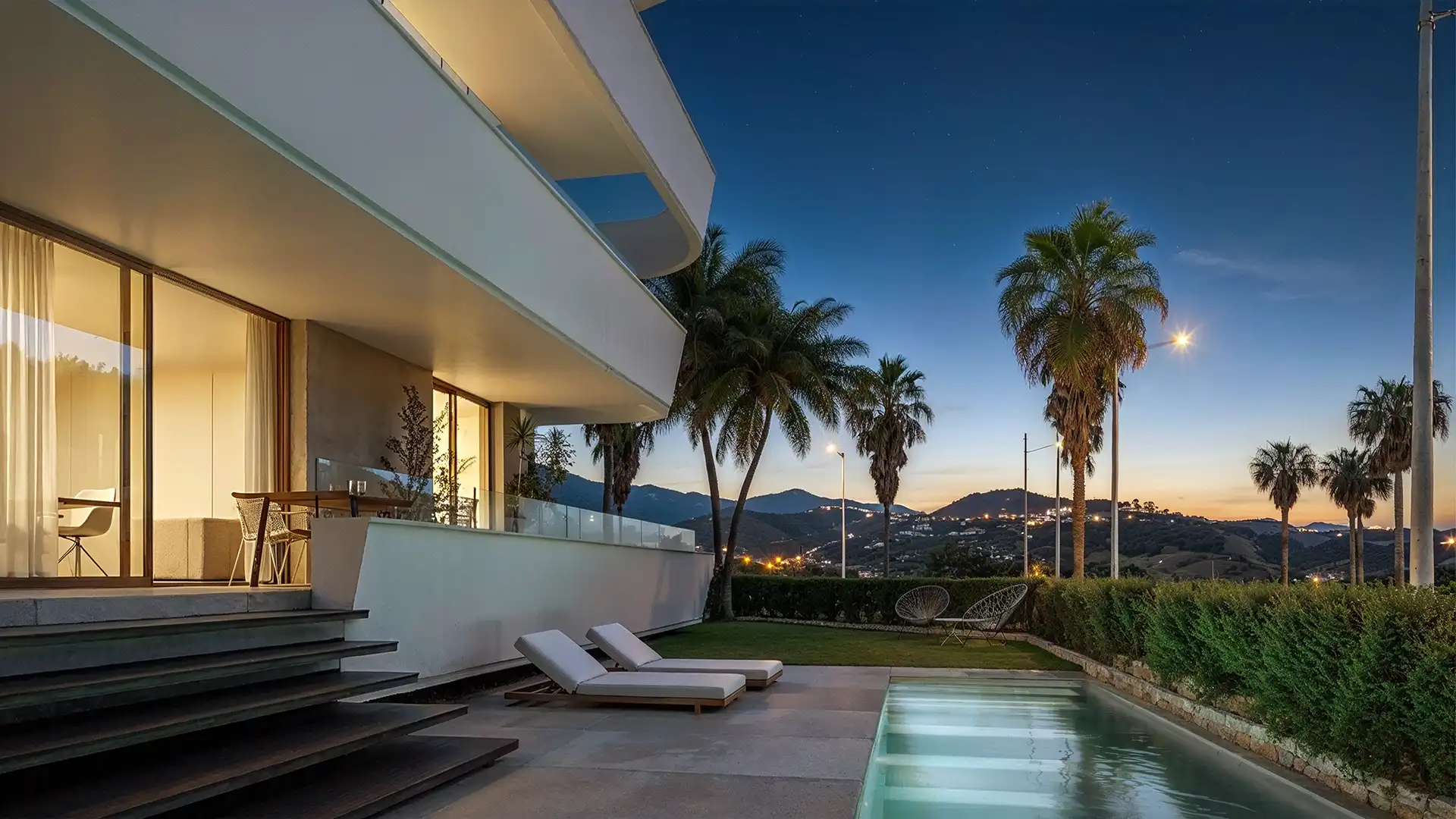 Contemporary Costa del Sol villa at dusk with lit terrace, palms, pool and hillside views